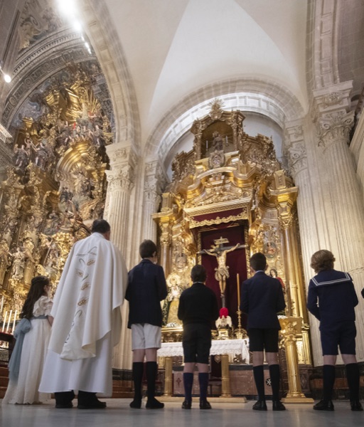 El sacerdote y cinco ninos de espaldas ante el altar dorado durante una primera comunion en Sevilla