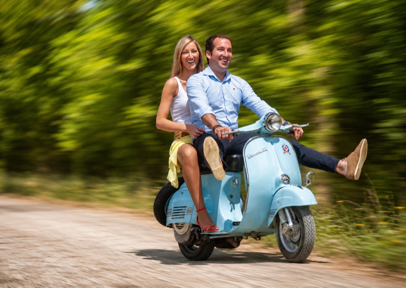Preboda en Vespa: ella con los brazos abiertos en marcha por un camino entre chopos